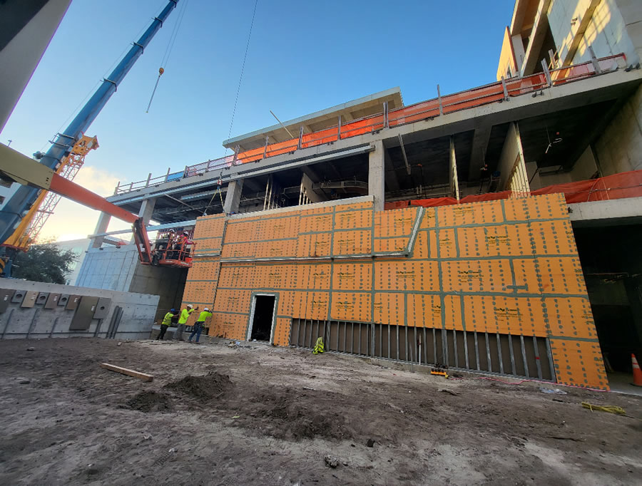 Image 7: A panel is hoisted into place. The image shows variations in feature detailing and panel sizes that accommodate multiple as-built condition constraints. It also shows a partially erected panel elevation in the upper right, a result of the required out-of-phase erection sequence. Courtesy of KENPAT.